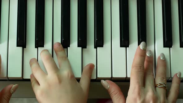 hands of a child and a woman playing the piano key