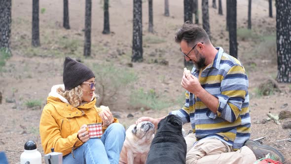 couple of two happy people and two dogs eating together doing a picnic on the ground