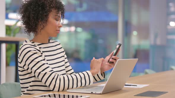 African Woman Using Smartphone and Laptop in Office