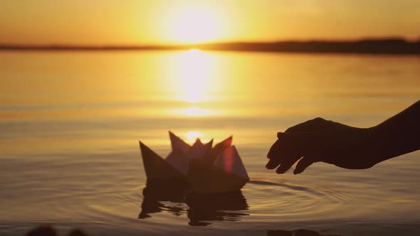 Human Hand is Launching Handmade Paper Boats Into the Lake at Sunset