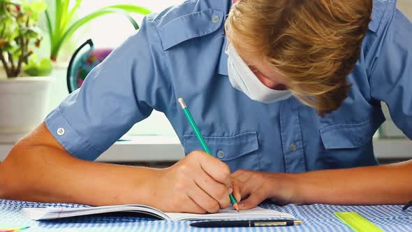 Teenage Man in a Blue Medical Mask of Caucasian Ethnicity Sits at His Desk at His Desk 