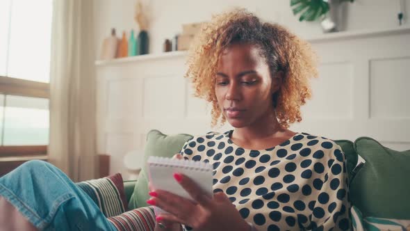 Thoughtful Woman Plans List of Goals and Tasks By Writing Them in Notebook