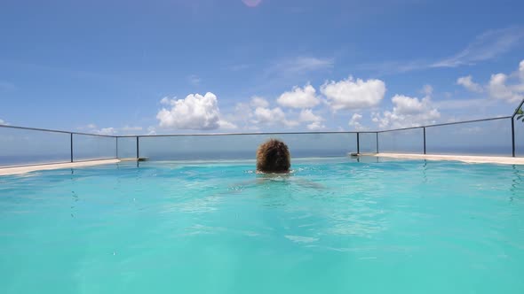 Camera Following Female Swimming in an Infinity Pool Overlooking an Ocean
