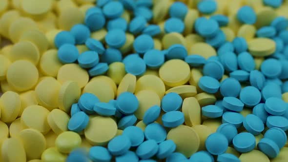 Small Blue Pills Falling From Above on Yellow Medicine Closeup