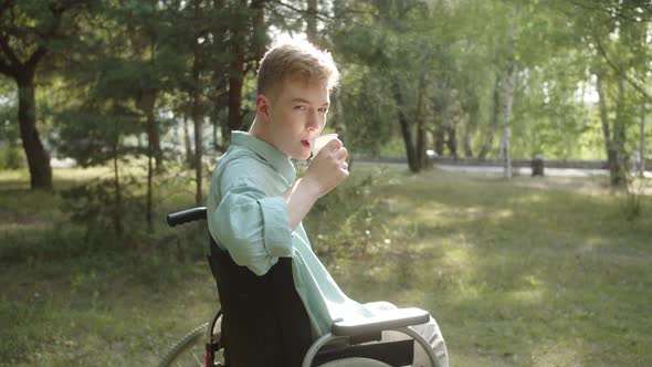 A Young Disabled Man in a Blue Shirt is Drinking His Beverage and Looking at the Camera and Smiling