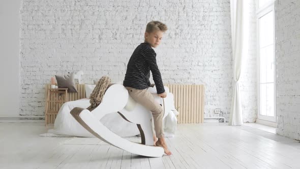 Little Child Boy Is Swinging on Rocking Horse in Nursery Playing in Free Time.