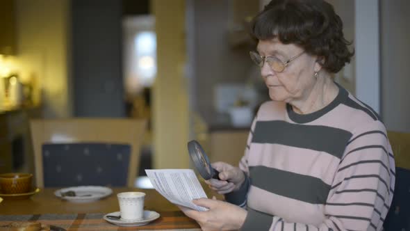 Senior Woman Reading Paper with Magnifying Glass at Home