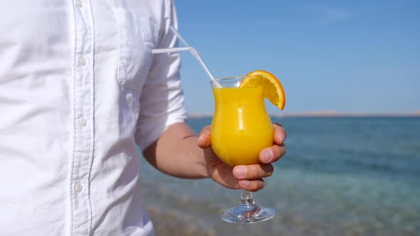 Man Hand Holding Fresh Orange Juice On The Beach By The Sea