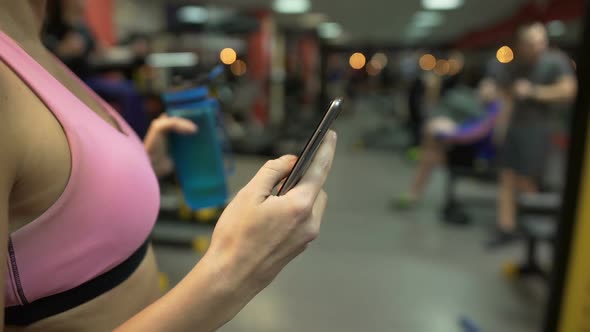 Girl Having Break From Exercise in Gym, Checking Cellphone, Water Bottle in Hand