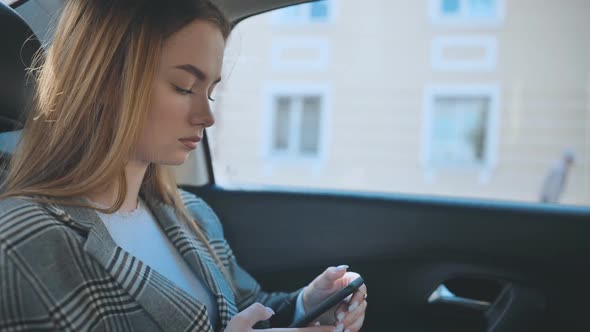 A Young Girl Rides in the Backseat of a Car and Watches Her Smartphone