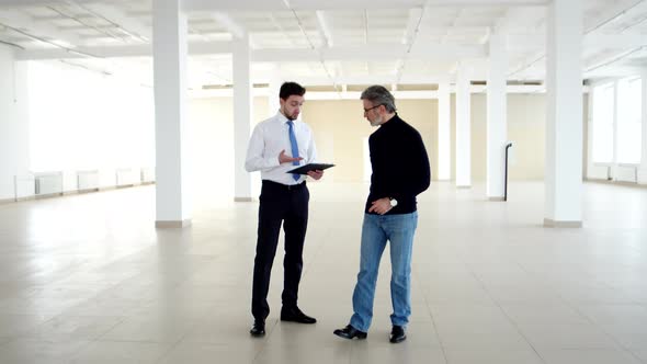 Businessman and Realtor Walk Through Office Space and Discuss Terms of Lease Front View