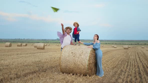 Happy Family with Male Child Standing on a Haystack Launch Paper Plane and Clap Their Hands