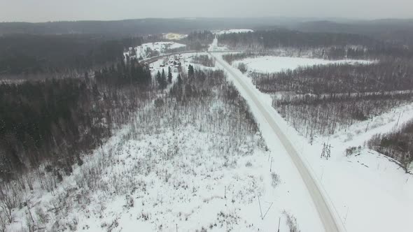 Flying Above Rural Road Through Forest In Bad Winter Cloudy Day With Snowfall