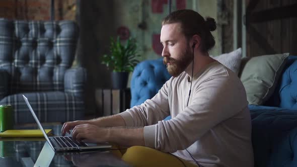 Man at Home Typing on Laptop Listening to Music in Headphones