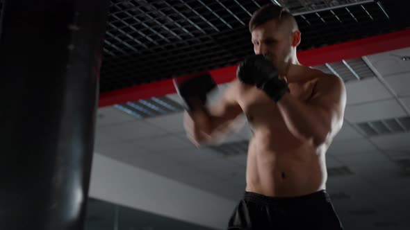 Masculine Caucasian Sportsman with Naked Torso Boxing Punching Bag in Gym