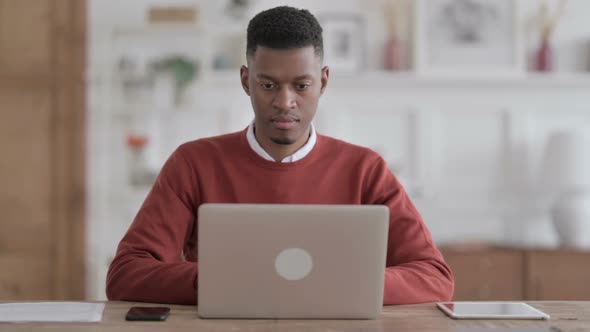 African Man Shaking Head as No Sign while using Laptop in Office