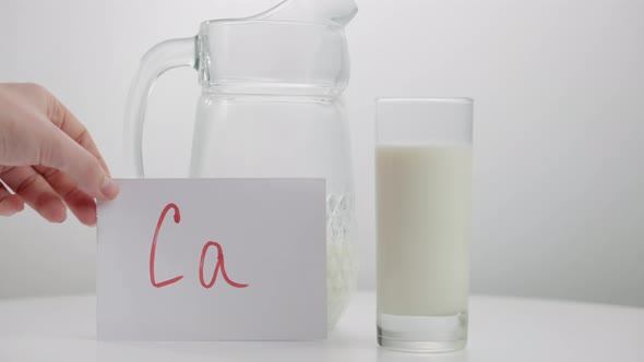 Closeup Jag and Glass with Organic Healthful Milk on Table and Female Hand Putting Ca Message