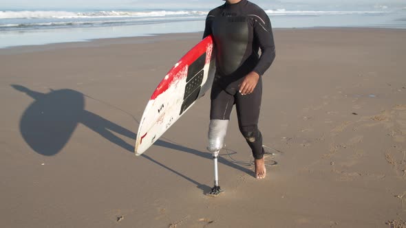 Tracking Shot of Surfer with Disability Walking Along Beach