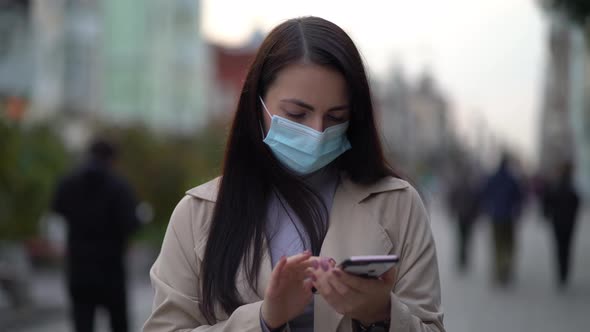 Portrait Woman in Protective Medical Mask Walks Down To the Street Uses Phone Texts Scrolls Surfs