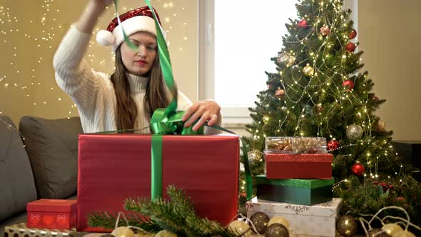 Pretty Brunette Woman in a Santa Hat Is Happily Unpacking Her Christmas Present
