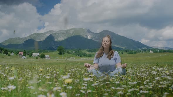 Woman relaxing and meditating outdoor while sitting in flower field