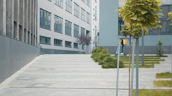 Lady Delivery Worker with Backpack and Yellow Cap Rides Electric Scooter Along