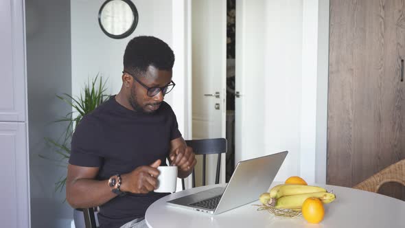 Confident African Man Work on Laptop at Home While Wife Is Busy in the Kitchen