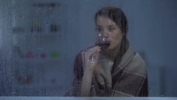 Pensive Woman in Blanket Drinking Wine Behind Rainy Window Cold Evening