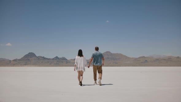 Back View Romantic Couple Walk Together Holding Hands Towards Epic White Flat Land in the Middle