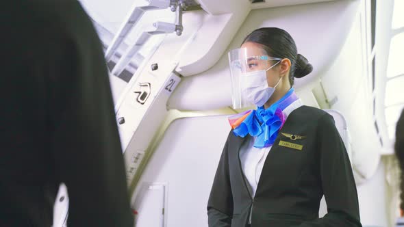 Asian flight attendants woman wearing face mask greeting passengers walking on board in airplane.