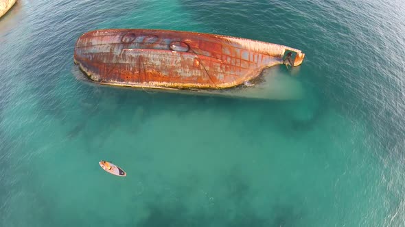 Aerial shot of young woman sup standup paddleboarding near a shipwreck in the Caribbean.