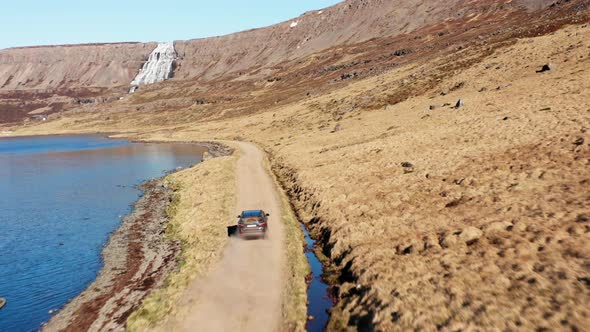 Car On Dirt Track By Fjord Towards Waterfall On Mountain