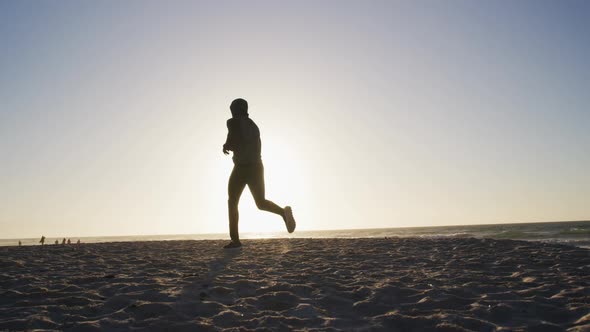 African american man running on beach, exercising outdoors in beach in the evening