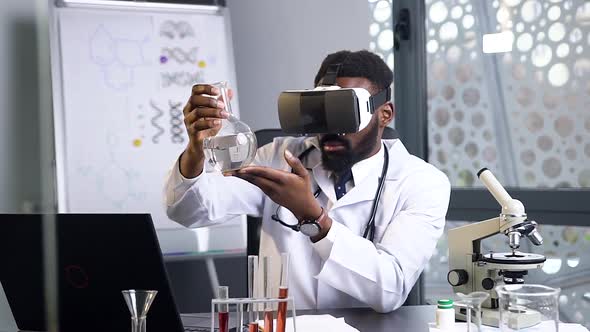 African American Male Doctor Looking at the Flask with Chemical Liquid Using Virtual Reality Headset