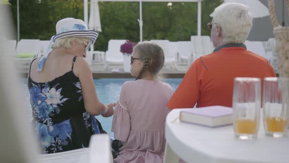 Grandmother, Grandfather and Grandchild Converse Sitting on the Edge of the Luxury Pool