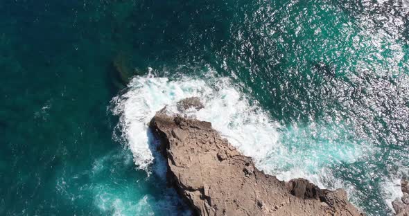 Aerial, tilt up, drone shot of waves hitting a rocky coast, blue sea, on a sunny day, in Mallorca, S