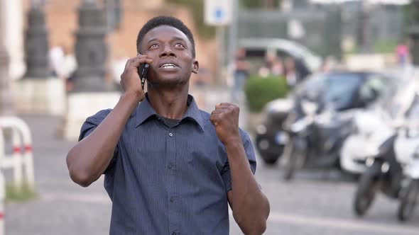 Happy african man rejoicing, he receives good news by phone- slow motion