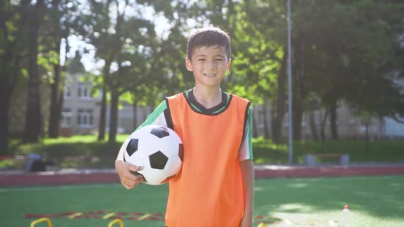 Asian Teen Boy in Football Wear Standing with Ball on the Stadium Among City Park Trees