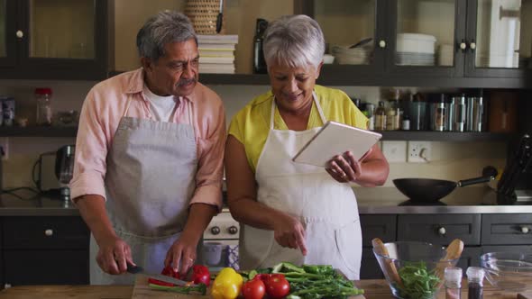 Senior mixed race couple using tablet preparing food in kitchen