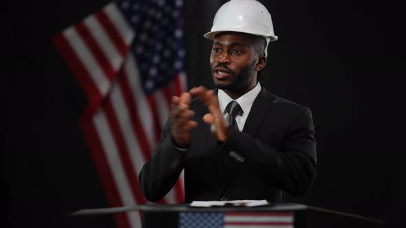 Positive African American Man in Suit and White Hard Hat Talking Gesturing and Smiling Presenting