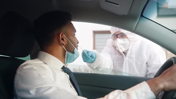 Medical Worker in Personal Protective Equipment Swabbing a Person in a Car Drive Through