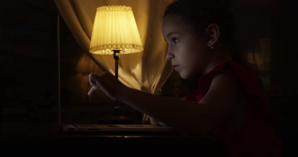 School Child, a Girl of 7-8 Years Old, Studies at Home Remotely in the Evening, Listens To School