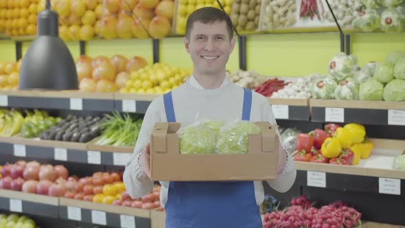 Portrait of Adult Caucasian Man Holding Box with Fresh Organic Cabbages and Smiling at Camera