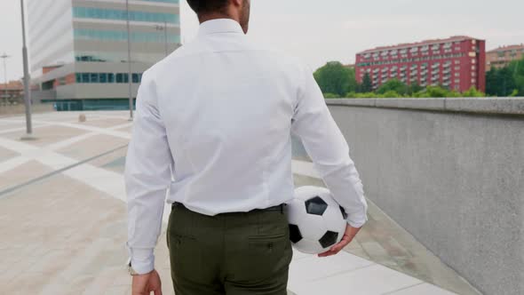 Businessman walking in the city carrying soccer ball