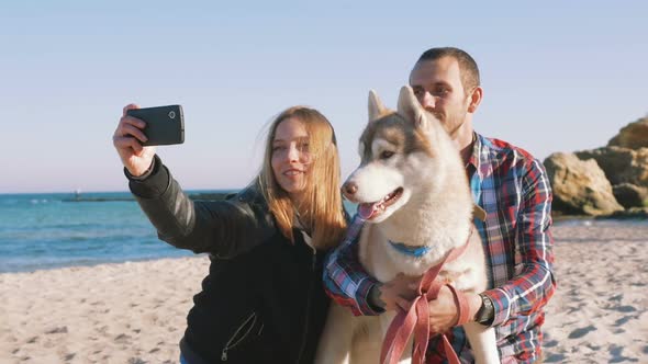 Young Caucasian Couple on Beach Doing Selfie on Smart Phone with Siberian Husky Dog Slow Motion