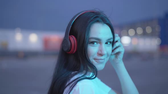 Close-up of Young Positive Woman in Blue Neon Lights Turning To Camera and Smiling. Portrait of