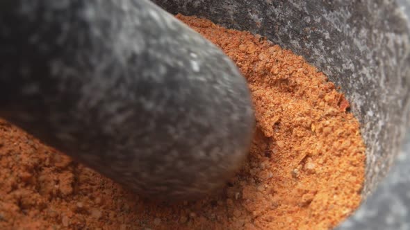 Closeup of Heavy Pestle Grinding and Mixing Spices and Peppers in the Mortar