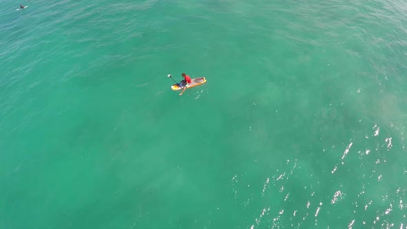 Aerial view of man sitting on board waiting for waves stand-up paddleboard surfing in Hawaii.