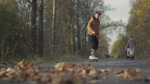 A Young Man with a Metal Prosthetic Leg Rides a Skateboard in an Autumn Park