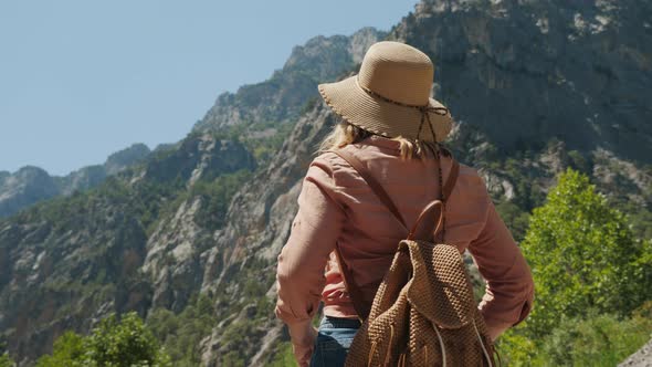 Woman Traveler in Hat and Backpack Enjoys Mountains